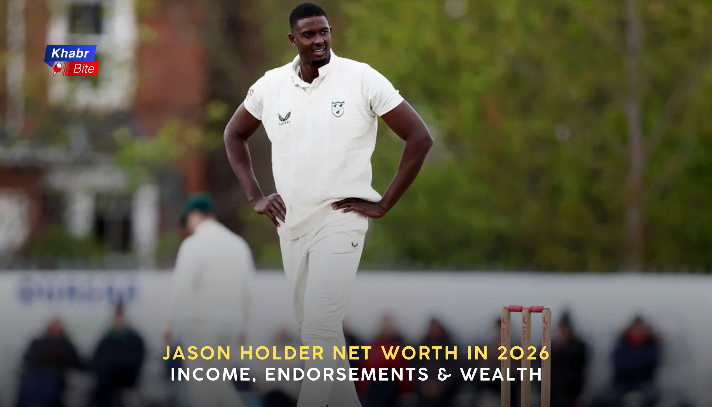 Jason Holder in white cricket uniform standing on the field with hands on hips.